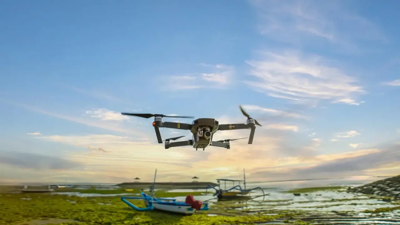 Un drone sorvola una spiaggia croata al tramonto, con barche tradizionali e alghe verdi sulla riva.