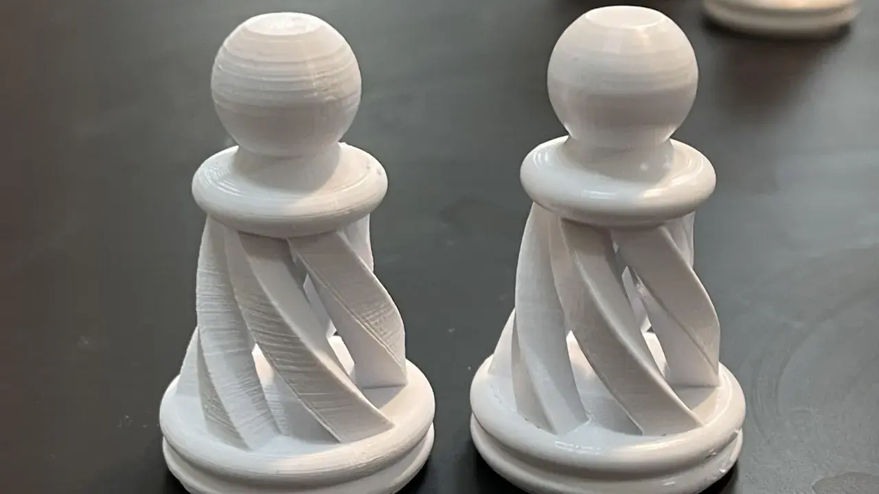 Due pedine degli scacchi bianche, stampate in 3D con filamento pla acetone, con un design a spirale.