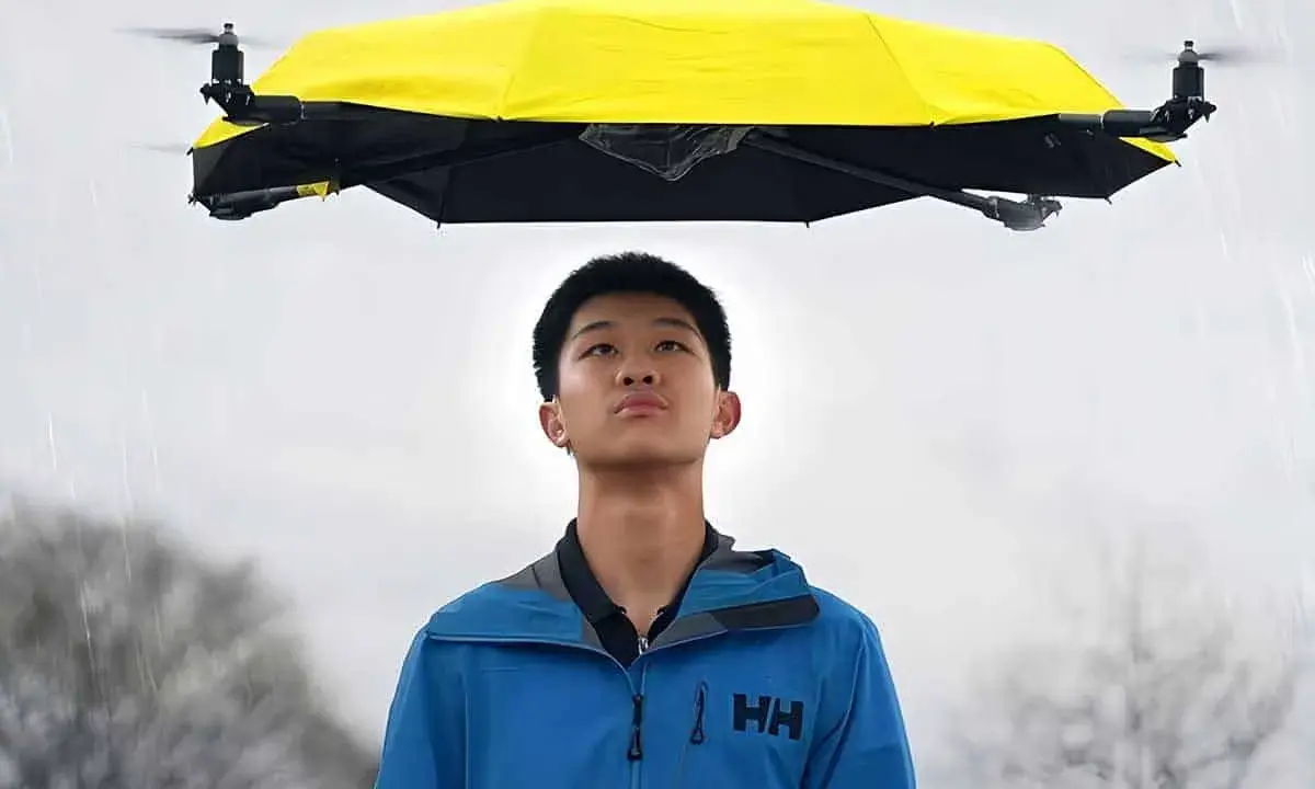Un ragazzo guarda un drone che vola con la pioggia, tenendo un ombrello giallo sopra di lui.