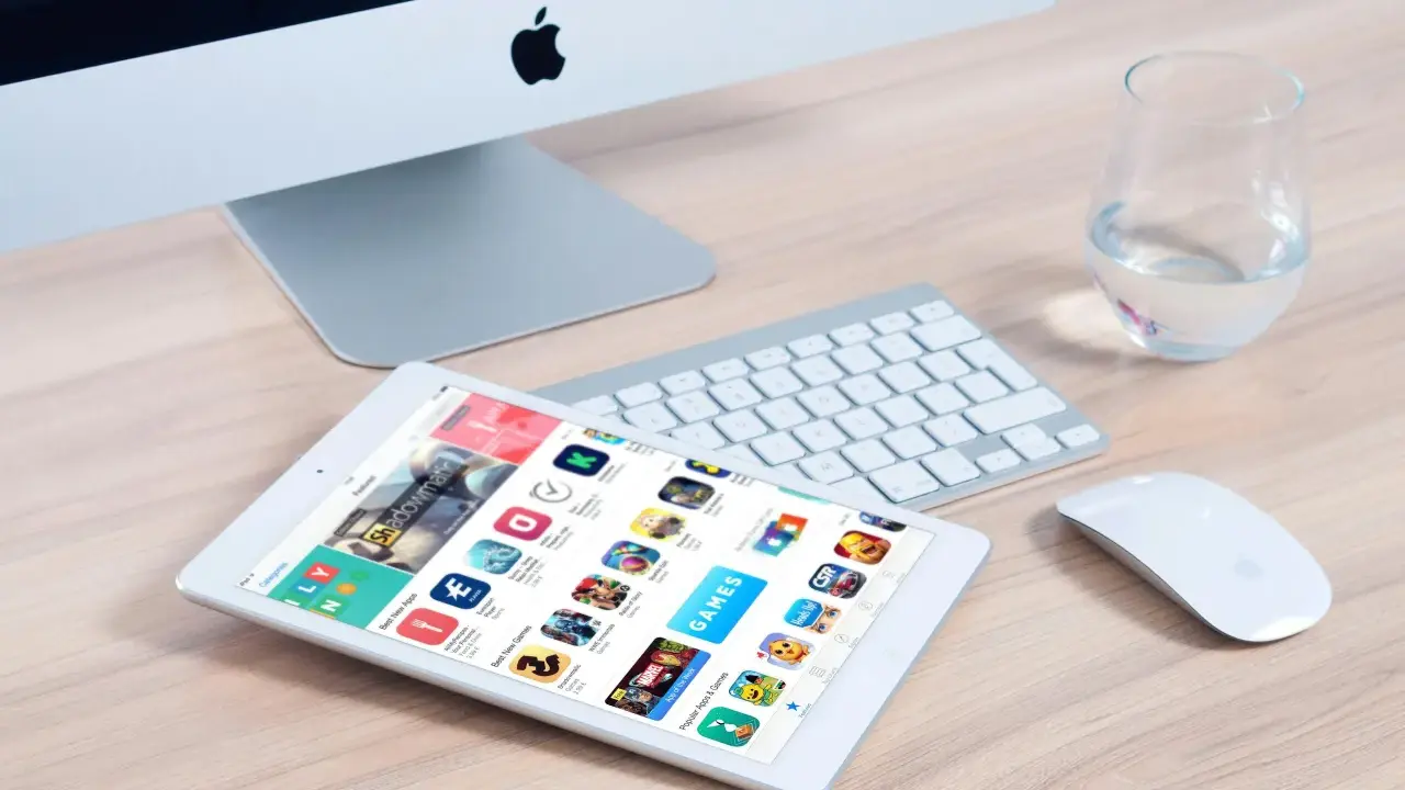Un tablet mostra l'App Store, con icone di giochi e app, suggerendo come creare app. Un iMac, tastiera e mouse completano la scena.