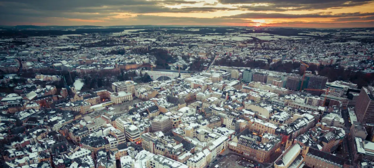 Vista aerea di un paesaggio urbano innevato al tramonto, con un drone che sorvola il Lussemburgo.
