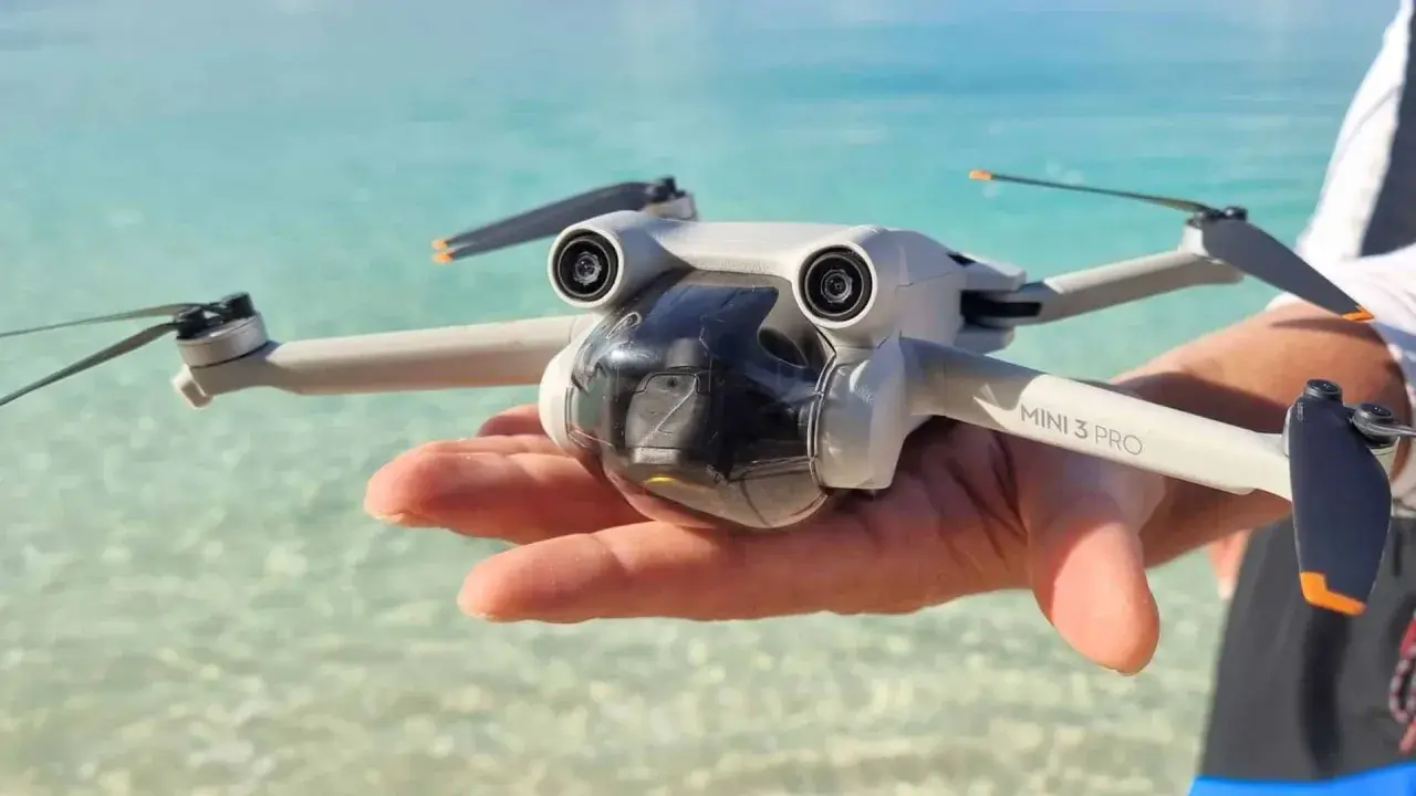 Un drone Mini 3 Pro tenuto in mano su una spiaggia tropicale, pronto per foto droni mozzafiato.