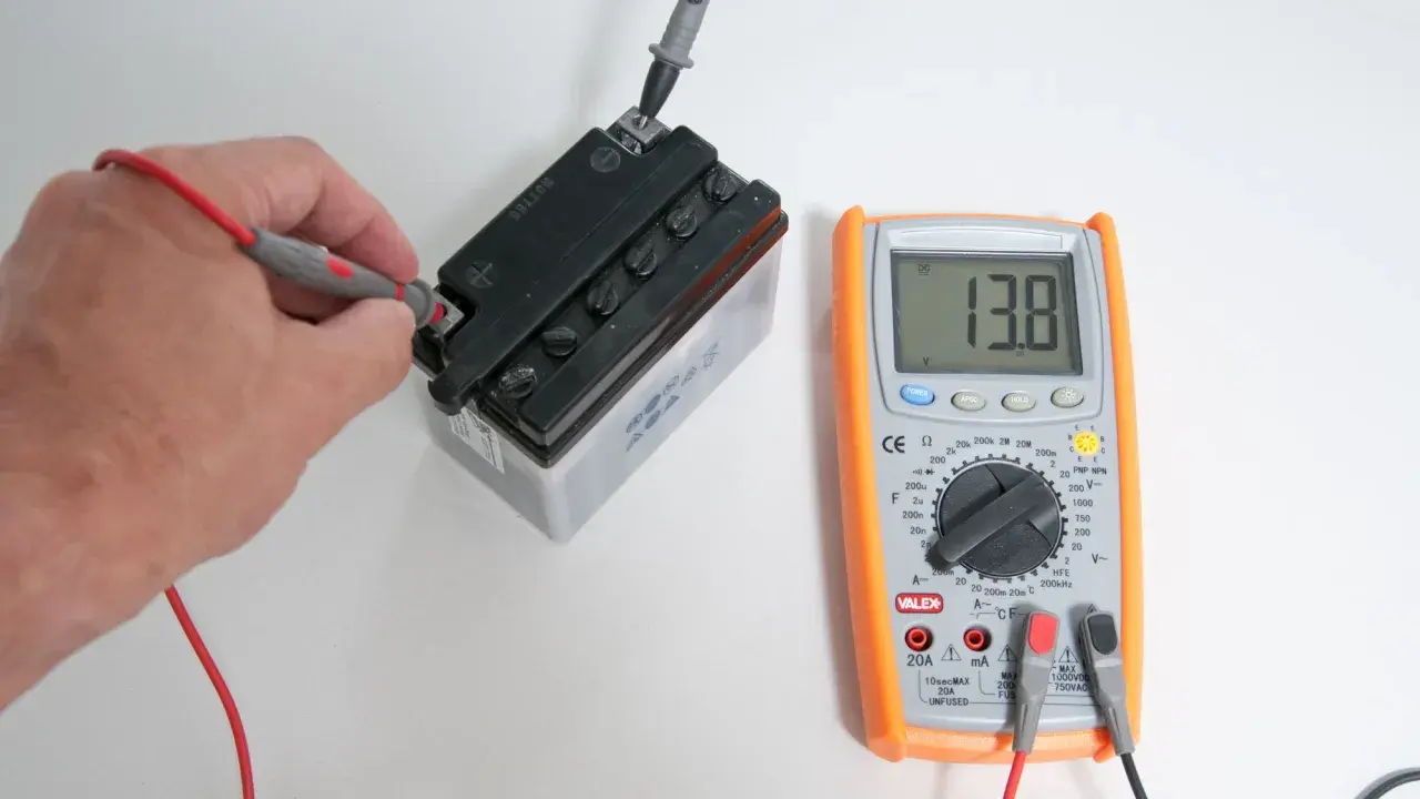 Mano che usa un tester per trovare la fase di una batteria, mostrando 13.8V.