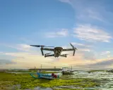 Un drone sorvola una spiaggia croata al tramonto, con barche tradizionali e alghe verdi sulla riva.