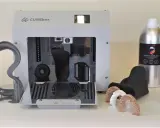 Flaconi di resina UV appiccicosa LIQCREATE, una stampante 3D CUREbox e vari modelli stampati, tra cui denti e un teschio.