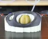 Stampa 3D di un oggetto con nucleo dorato, circondato da strati bianchi e una cornice esterna grigia. Il materiale di supporto PVA è visibile nei dettagli.