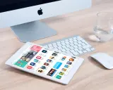 Un tablet mostra l'App Store, con icone di giochi e app, suggerendo come creare app. Un iMac, tastiera e mouse completano la scena.