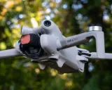 Il DJI Mini 4 Pro in uscita, con filtro rosso sulla fotocamera, vola tra gli alberi.
