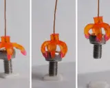 Un oggetto stampato in 4d, simile a un fiore arancione, si apre e si chiude attorno a un bullone, dimostrando la sua flessibilità.