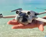 Un drone Mini 3 Pro tenuto in mano su una spiaggia tropicale, pronto per foto droni mozzafiato.