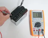 Mano che usa un tester per trovare la fase di una batteria, mostrando 13.8V.