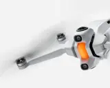 Un drone in volo, bianco e compatto, con eliche in rapido movimento e una luce arancione sul corpo.