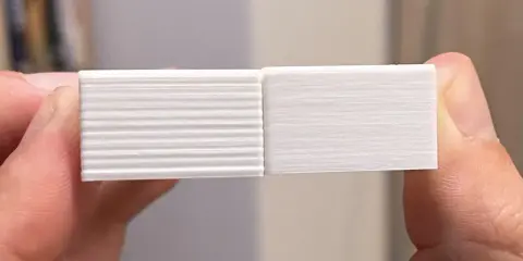 Due campioni stampati in 3D, uno con evidenti linee orizzontali dovute a z wobble, l'altro liscio.