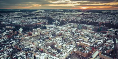 Vista aerea di un paesaggio urbano innevato al tramonto, con un drone che sorvola il Lussemburgo.