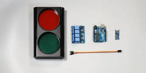 Componenti per un semaforo fai da te: un corpo con luci rosse e verdi, schede Arduino, un modulo relè e cavi.
