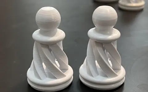 Due pedine degli scacchi bianche, stampate in 3D con filamento pla acetone, con un design a spirale.