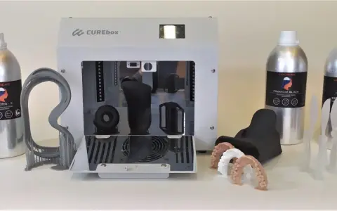Flaconi di resina UV appiccicosa LIQCREATE, una stampante 3D CUREbox e vari modelli stampati, tra cui denti e un teschio.