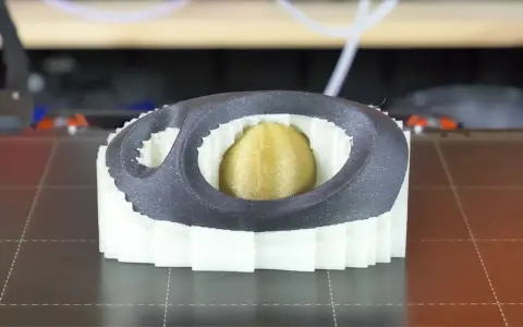 Stampa 3D di un oggetto con nucleo dorato, circondato da strati bianchi e una cornice esterna grigia. Il materiale di supporto PVA è visibile nei dettagli.
