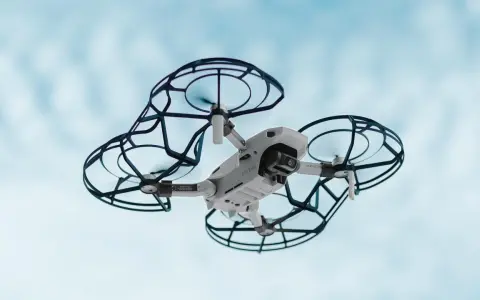 Un drone bianco con protezioni nere vola nel cielo azzurro. Perfetto per la tua scuola di droni.