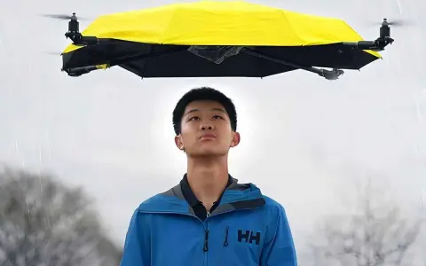 Un ragazzo guarda un drone che vola con la pioggia, tenendo un ombrello giallo sopra di lui.