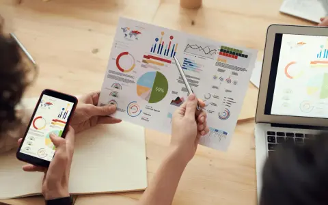 Persone analizzano grafici su fogli e smartphone, con un laptop aperto. Il software di programmazione aiuta a visualizzare dati complessi.
