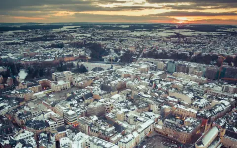 Vista aerea di un paesaggio urbano innevato al tramonto, con un drone che sorvola il Lussemburgo.