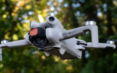 Il DJI Mini 4 Pro in uscita, con filtro rosso sulla fotocamera, vola tra gli alberi.