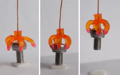 Un oggetto stampato in 4d, simile a un fiore arancione, si apre e si chiude attorno a un bullone, dimostrando la sua flessibilità.