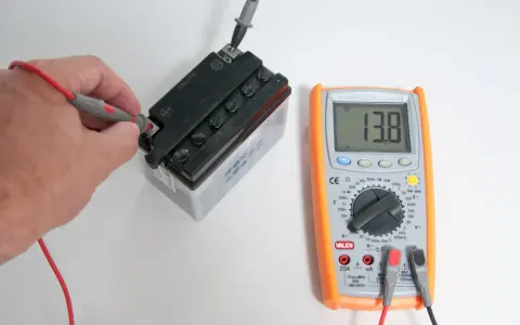 Mano che usa un tester per trovare la fase di una batteria, mostrando 13.8V.