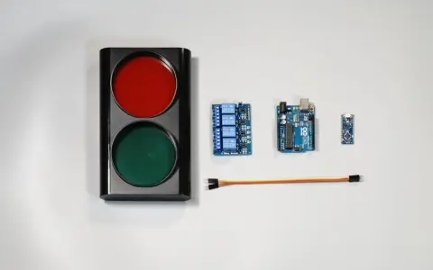 Componenti per un semaforo fai da te: un corpo con luci rosse e verdi, schede Arduino, un modulo relè e cavi.