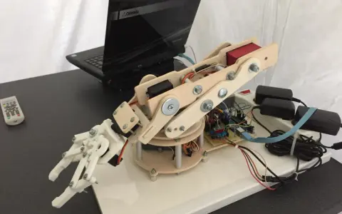 Mano robotica Arduino in legno e plastica, collegata a un laptop e alimentata da adattatori.
