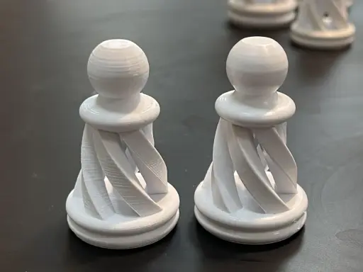 Due pedine degli scacchi bianche, stampate in 3D con filamento pla acetone, con un design a spirale.