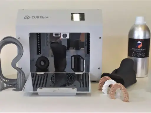 Flaconi di resina UV appiccicosa LIQCREATE, una stampante 3D CUREbox e vari modelli stampati, tra cui denti e un teschio.