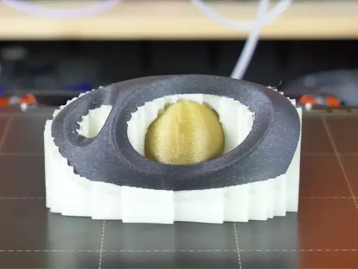 Stampa 3D di un oggetto con nucleo dorato, circondato da strati bianchi e una cornice esterna grigia. Il materiale di supporto PVA è visibile nei dettagli.
