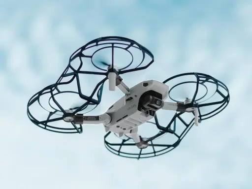 Un drone bianco con protezioni nere vola nel cielo azzurro. Perfetto per la tua scuola di droni.