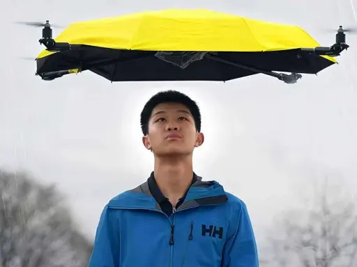 Un ragazzo guarda un drone che vola con la pioggia, tenendo un ombrello giallo sopra di lui.