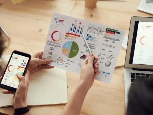 Persone analizzano grafici su fogli e smartphone, con un laptop aperto. Il software di programmazione aiuta a visualizzare dati complessi.