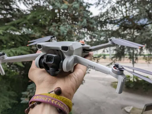 Un drone DJI Mini 3 Pro, perfetto per chi cerca un drone DJI senza patentino, tenuto in mano con alberi sullo sfondo.