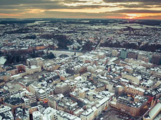 Vista aerea di un paesaggio urbano innevato al tramonto, con un drone che sorvola il Lussemburgo.
