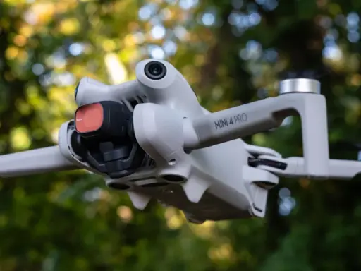Il DJI Mini 4 Pro in uscita, con filtro rosso sulla fotocamera, vola tra gli alberi.