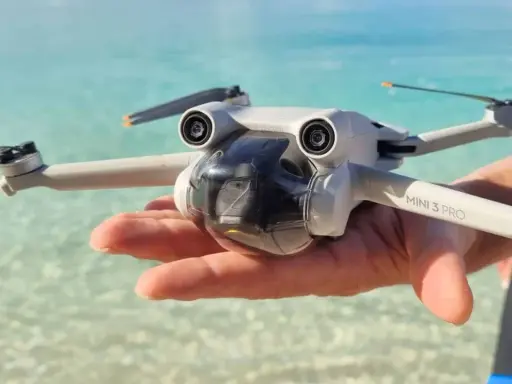 Un drone Mini 3 Pro tenuto in mano su una spiaggia tropicale, pronto per foto droni mozzafiato.