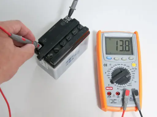 Mano che usa un tester per trovare la fase di una batteria, mostrando 13.8V.