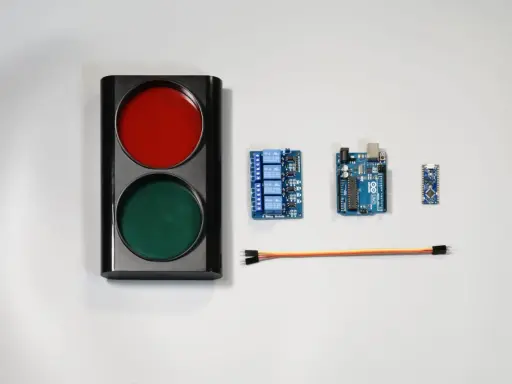 Componenti per un semaforo fai da te: un corpo con luci rosse e verdi, schede Arduino, un modulo relè e cavi.