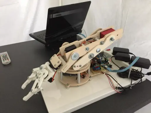 Mano robotica Arduino in legno e plastica, collegata a un laptop e alimentata da adattatori.