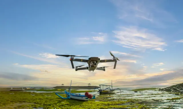 Un drone sorvola una spiaggia croata al tramonto, con barche tradizionali e alghe verdi sulla riva.