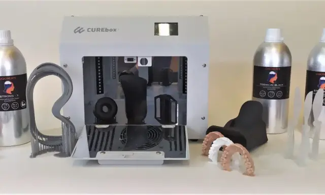 Flaconi di resina UV appiccicosa LIQCREATE, una stampante 3D CUREbox e vari modelli stampati, tra cui denti e un teschio.
