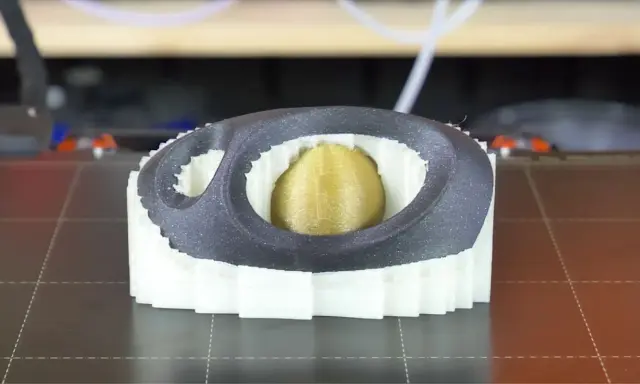 Stampa 3D di un oggetto con nucleo dorato, circondato da strati bianchi e una cornice esterna grigia. Il materiale di supporto PVA è visibile nei dettagli.