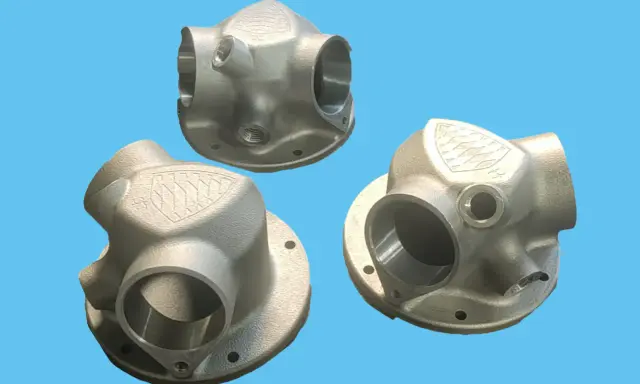 Tre componenti metallici complessi, realizzati con stampa 3D acciaio, mostrano un design intricato con diverse aperture e un logo inciso.