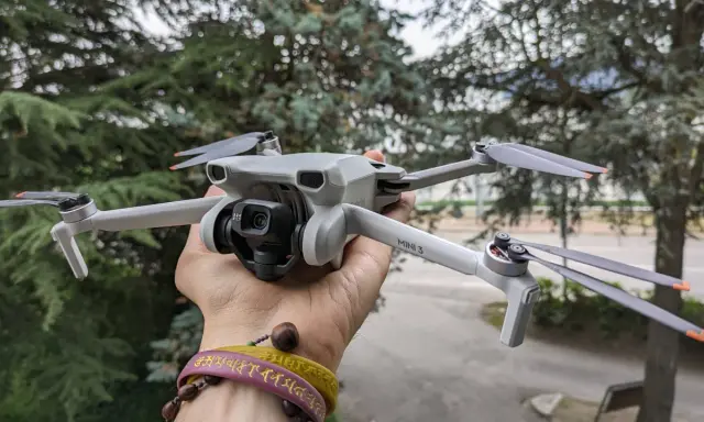 Un drone DJI Mini 3 Pro, perfetto per chi cerca un drone DJI senza patentino, tenuto in mano con alberi sullo sfondo.