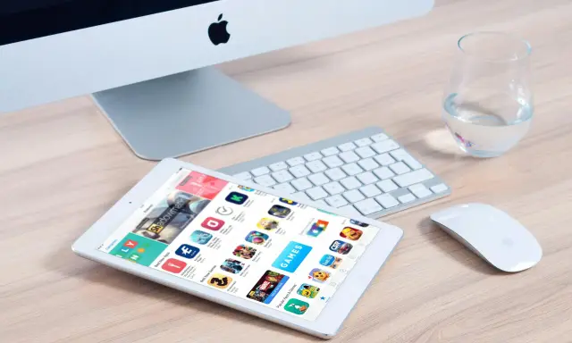 Un tablet mostra l'App Store, con icone di giochi e app, suggerendo come creare app. Un iMac, tastiera e mouse completano la scena.